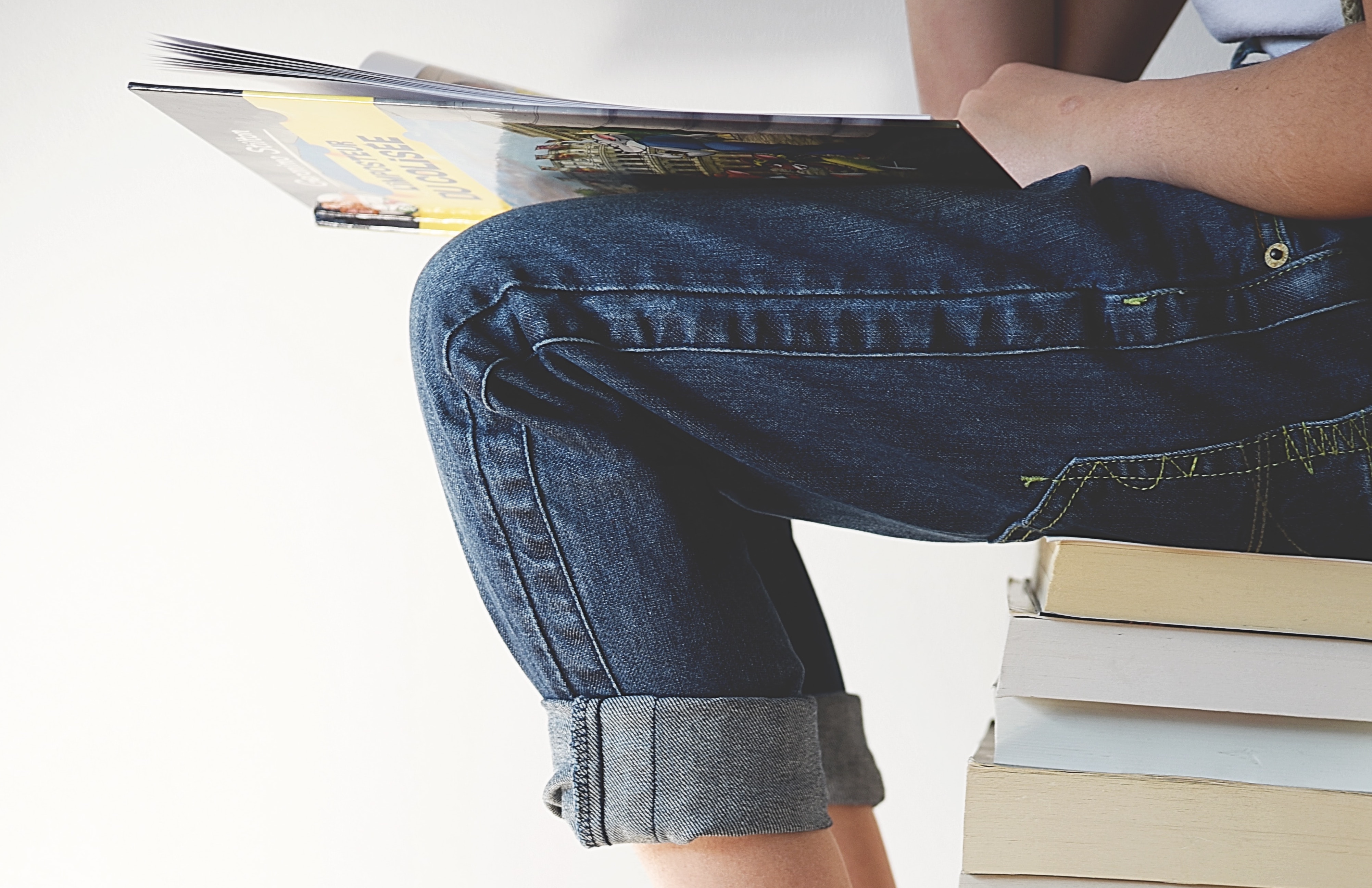 Person sitting on stack of paper-back books