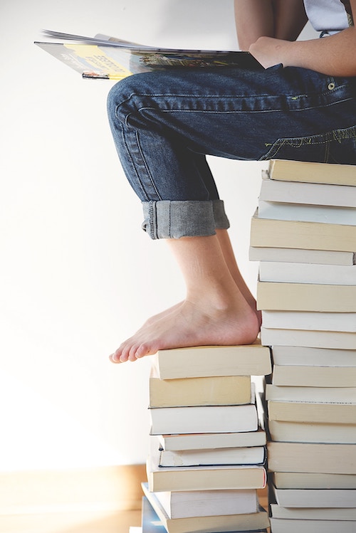 Person sitting on stack of paper-back books