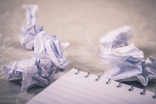 A spiral bound, lined notebook in the foreground with several balls of crumpled up paper just beyond it.